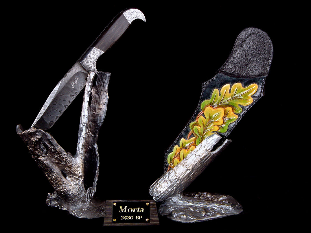 "Morta" in twist damascus welded blade, hand-engraved 304 stainless steel bolsters, ancient Bog Oak handle, hand-carved, hand-dyed leather sheath, hand-cast bronze stands