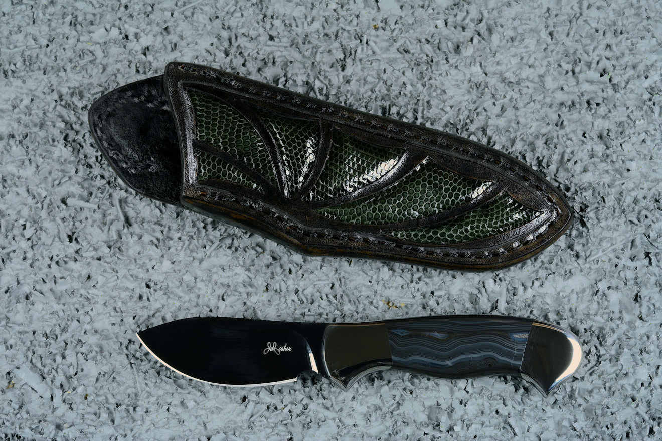 "Ullr", (with reflector above), obverse side view in deep cryogenically treated O1 tungsten-vanadium alloy tool steel blade, 304 stainless steel bolsters, Silver Crown Psilomelane gemstone handle, hand-carved leather sheath inlaid with gray lizard skin