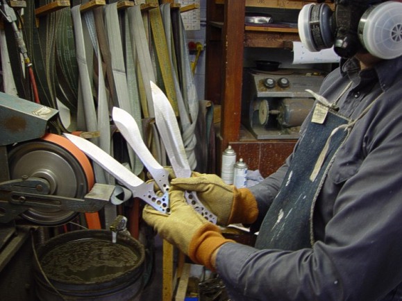 Master grinds: Jay holding three hollow ground tactical combat style blades at the belt grinder.
