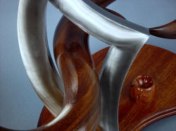 "Tribal" knife display sculptural stand, triangle of stainless steel pierced by walnut hardwood hand-carved form exhibits stark material contrast