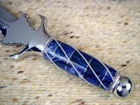 Sodalite gemstone, polished, carved, and inlaid with wire. There are 40 pieces in this knife handle, many of them hidden are used for structural integrity